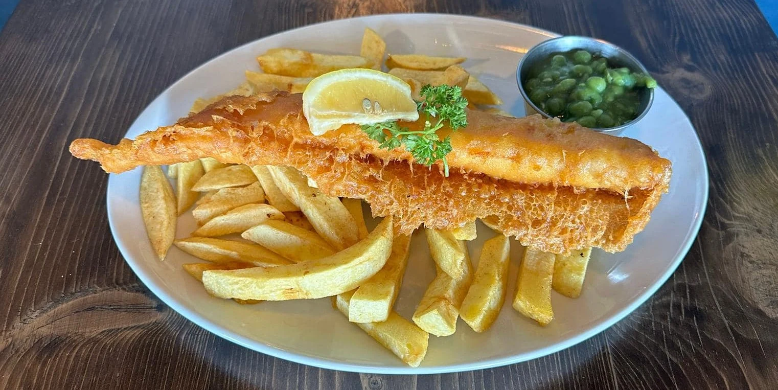 Golden battered fish with chips, peas and lemon